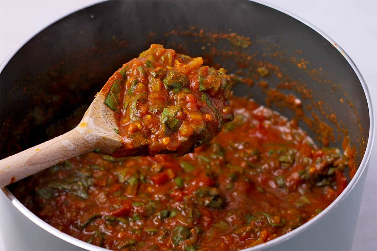Indian curry sauce with tomatoes and chopped spinach and a wooden spoonful of sauce.