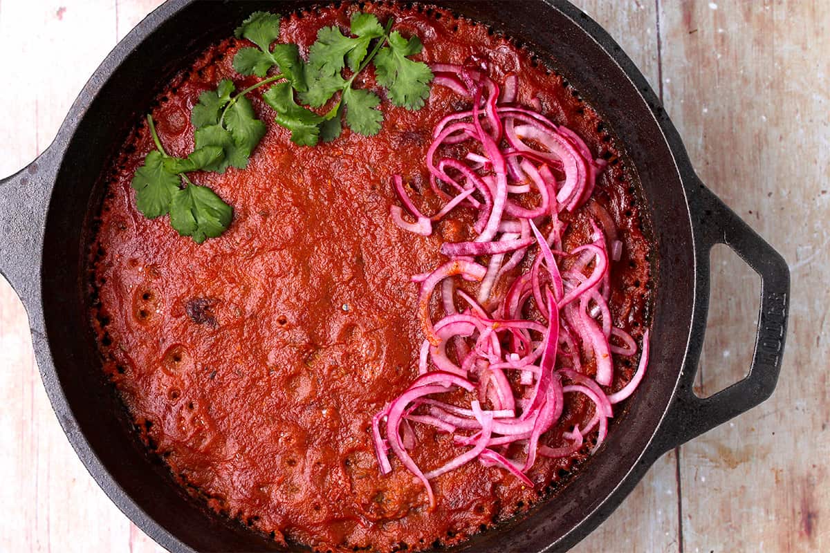 Baked kidney bean curry in a cast iron pot with sliced red onions and cilantro on top.