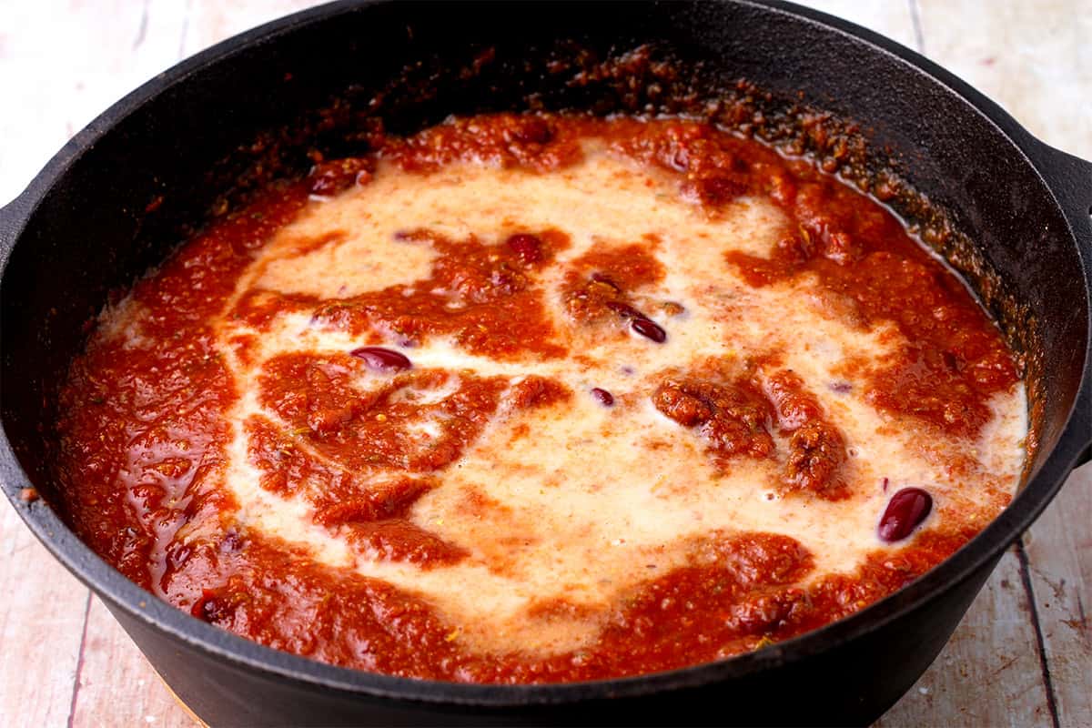 Plant milk, kidney beans, and tomato sauce in a black pan.