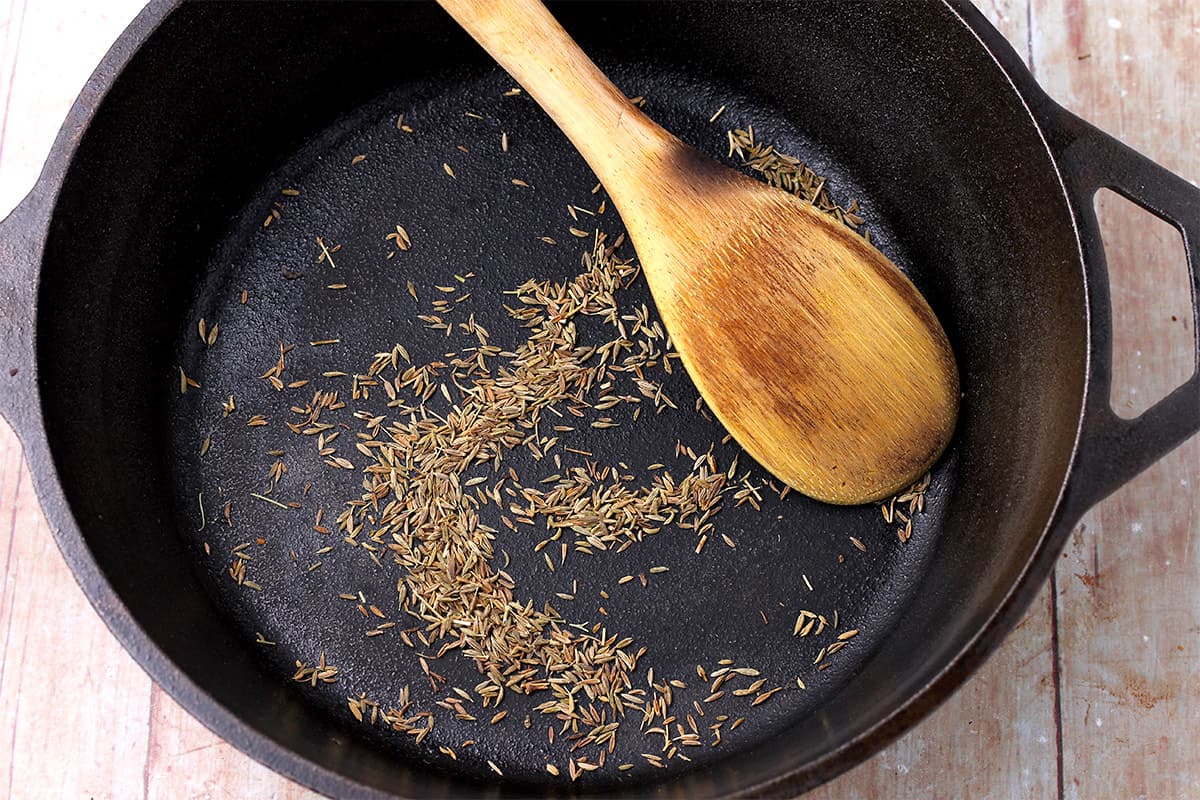 Cumin seeds are toasted in a cast iron skillet.