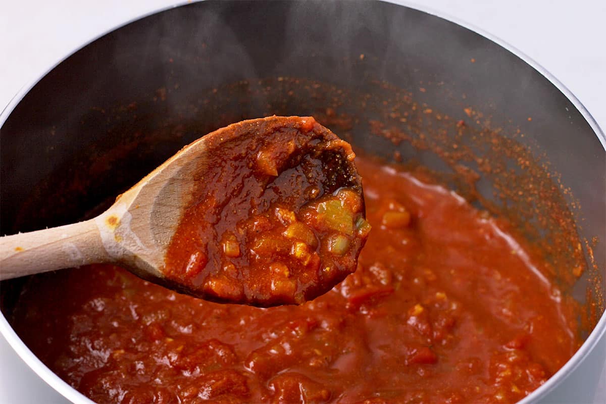 Tomato sauce with onions in a saucepan with a wooden spoon.