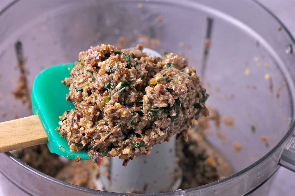 Mushroom kale burger mixture over a food processor in a spatula.