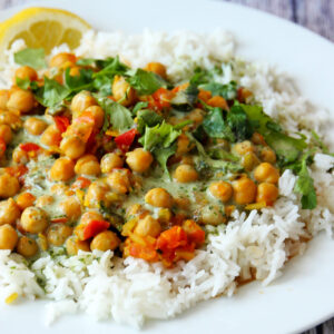 A closeup of chickpea curry with tomatoes and cilantro sauce over white rice.