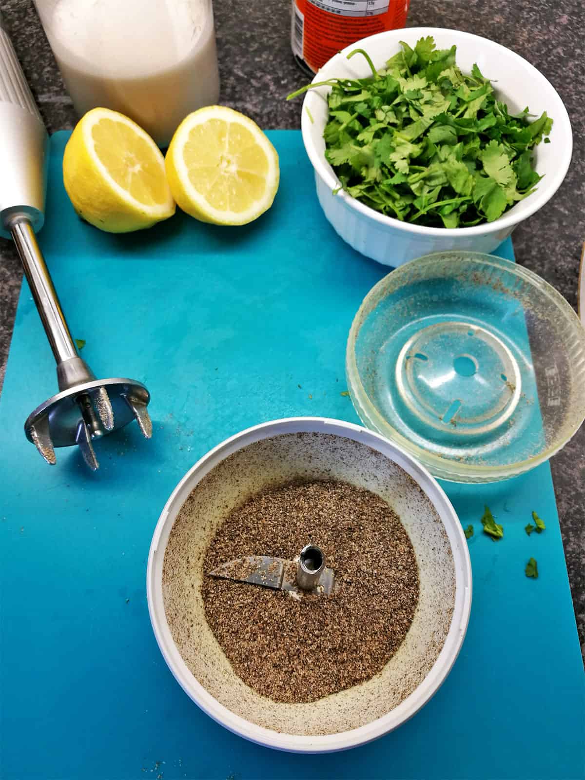 Ground flax seeds in a spice grinder with fresh cilantro, a cut lemon, and coconut milk.