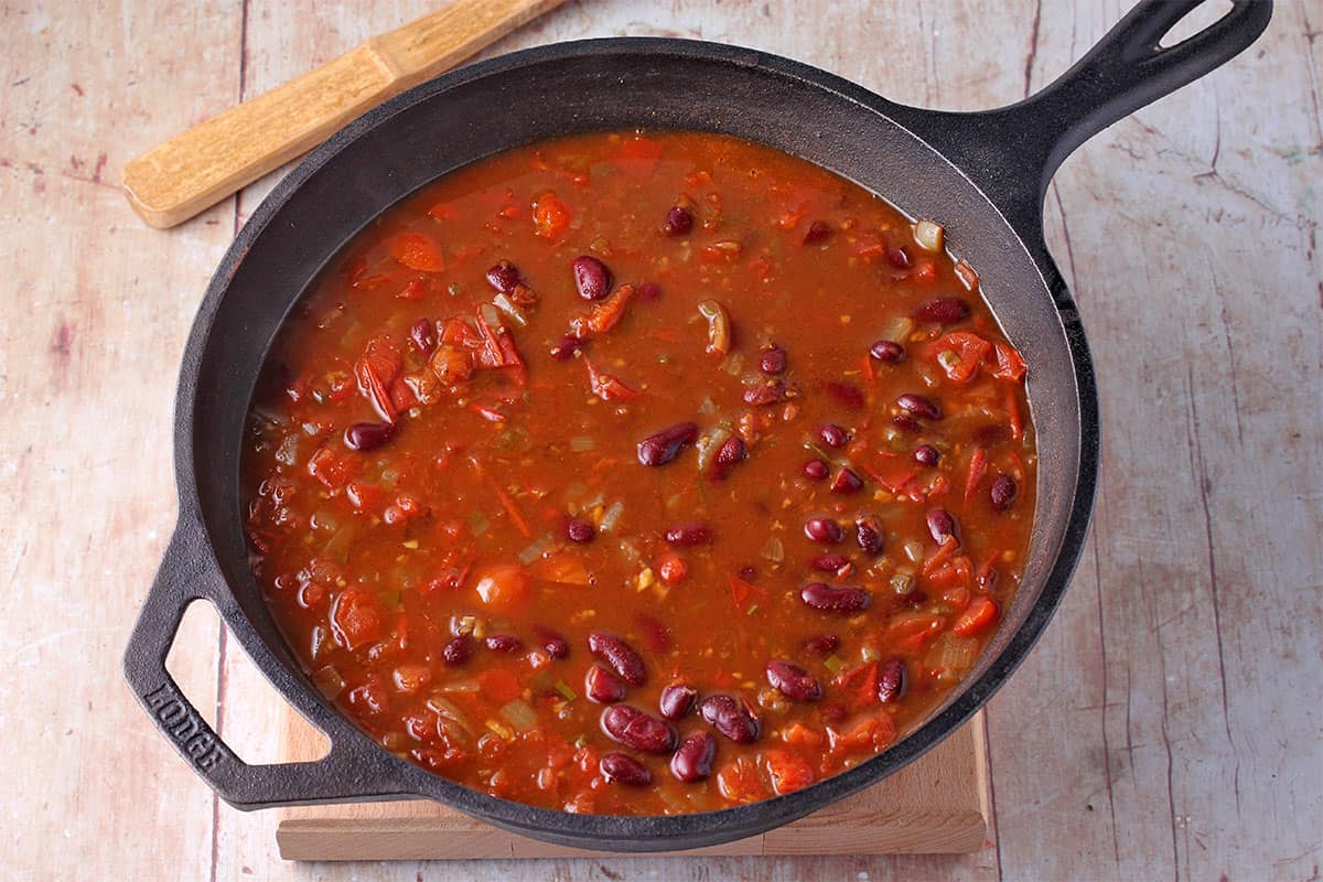 Kidney bean curry in a black cast iron pot sitting on a wooden block.