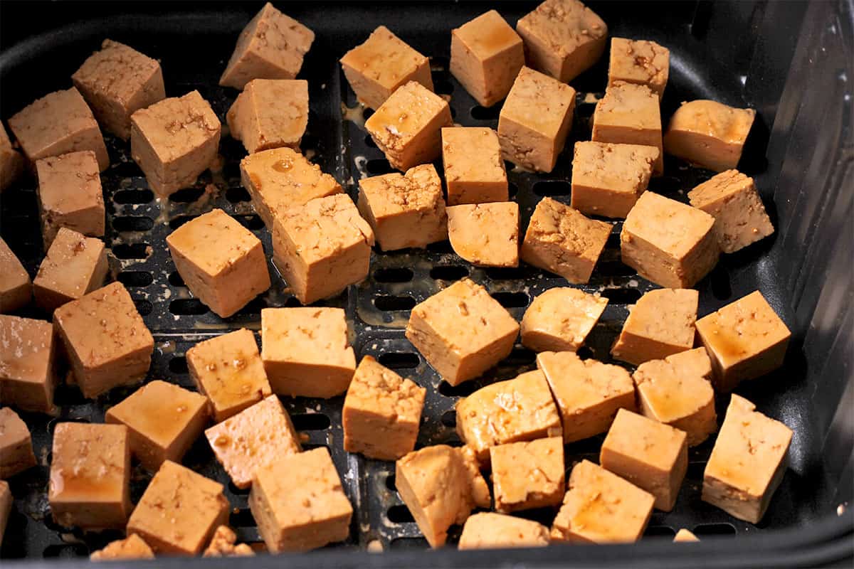 Uncooked tofu cubes with soy sauce and cornstarch in the air fryer basket.