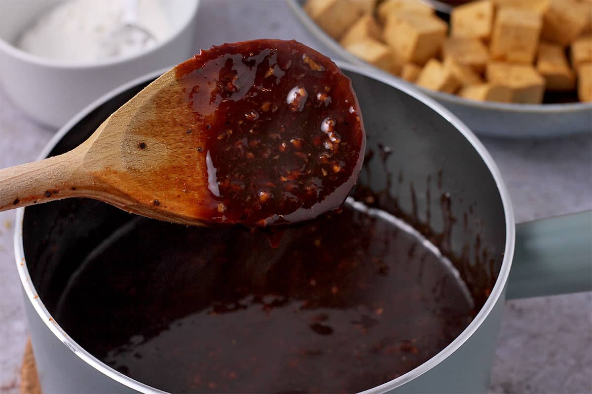 Brown Mongolian sauce in a wooden spoon held over a blue saucepan.