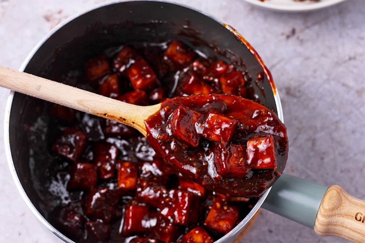 Tofu cubes are mixed with Mongolian sauce in a saucepan.