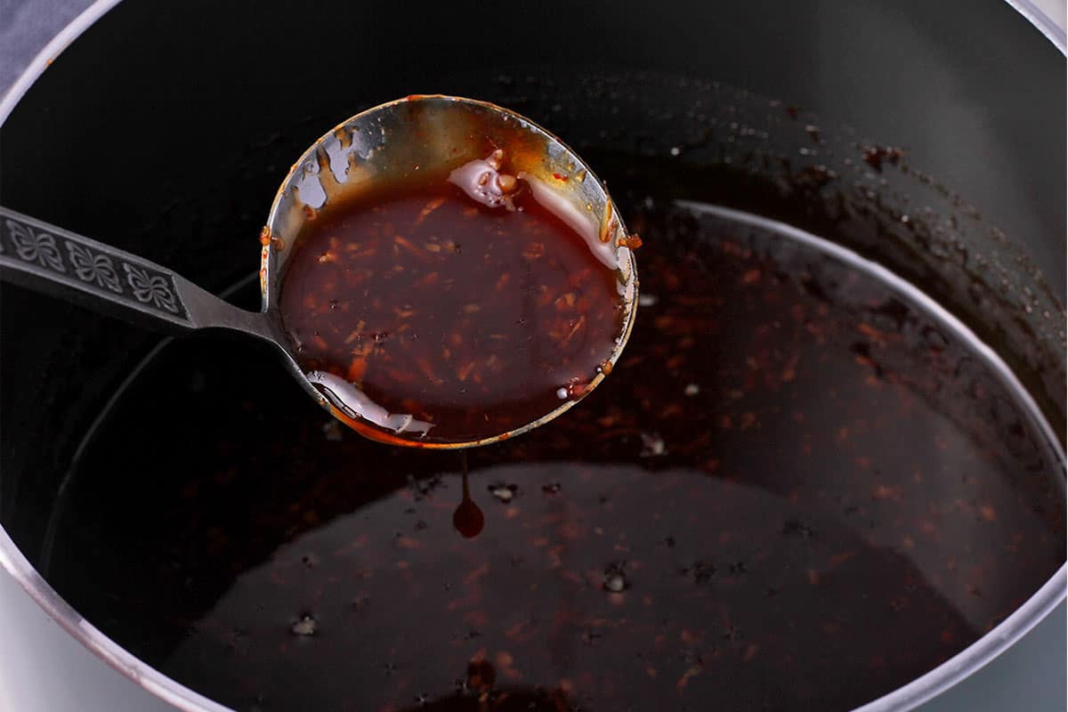 A ladle of sriracha dipping sauce held over a saucepan.