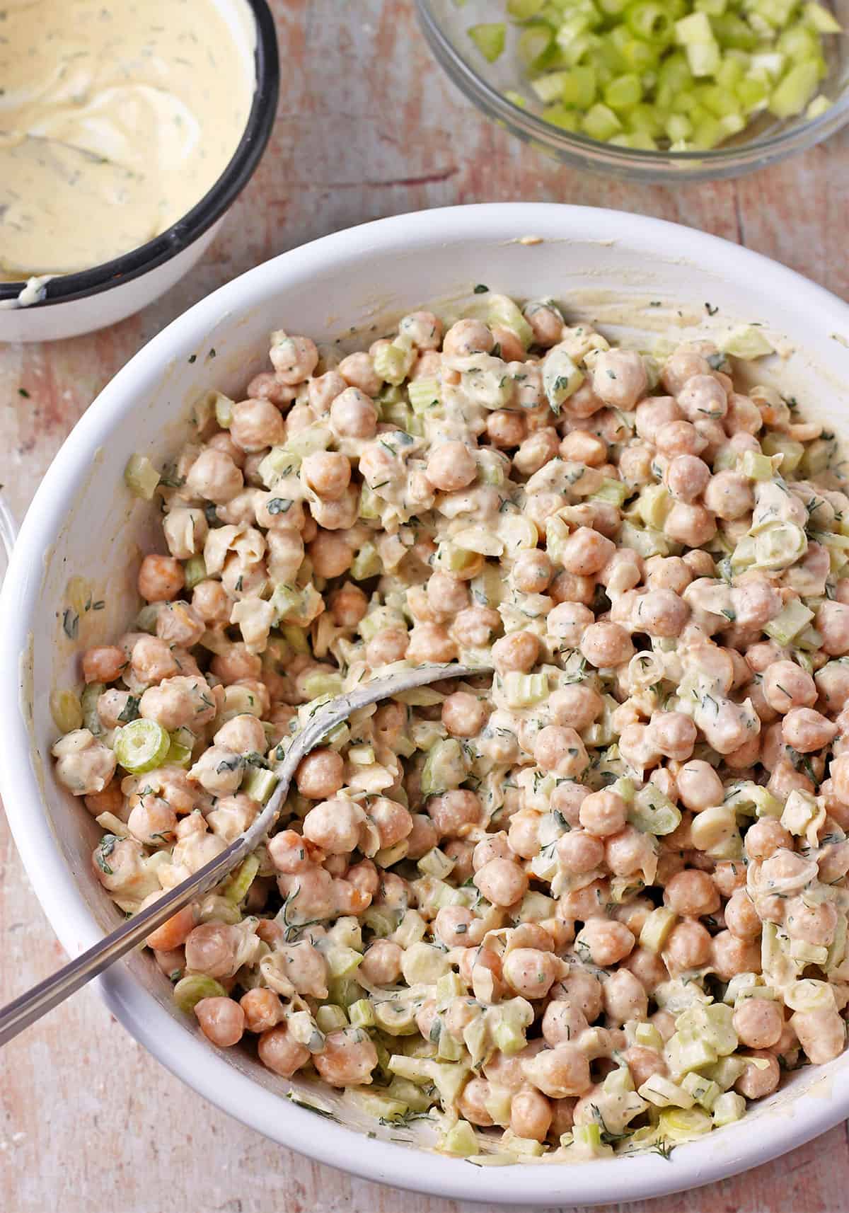 Creamy chickpea salad with celery and green onions in a white bowl with a spoon.