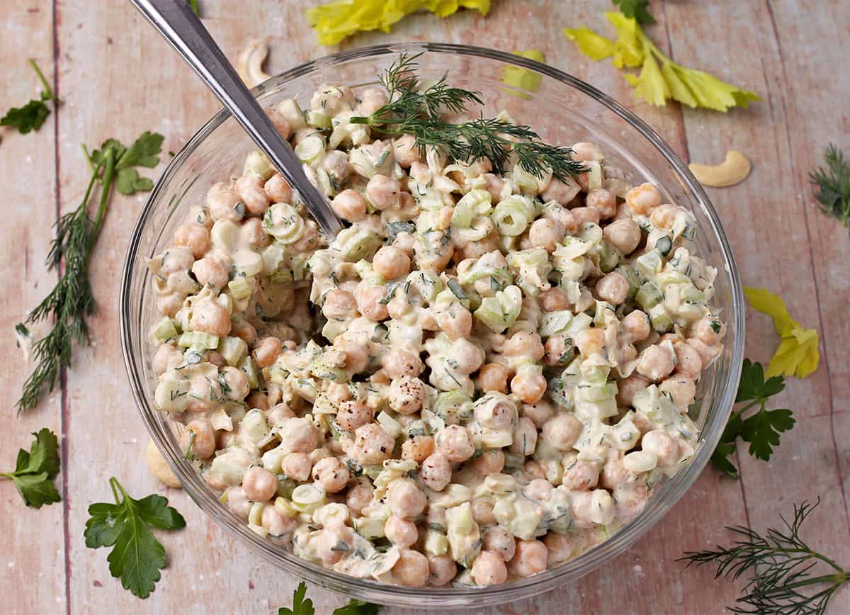 Chickpeas in a creamy dressing with green onions and celery in a glass bowl.