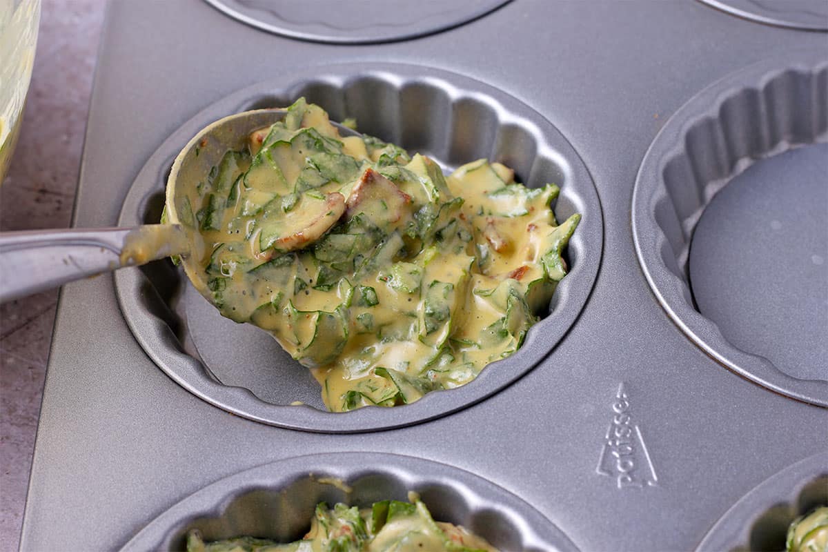 Vegan quiche batter is spooned into a muffin tin.