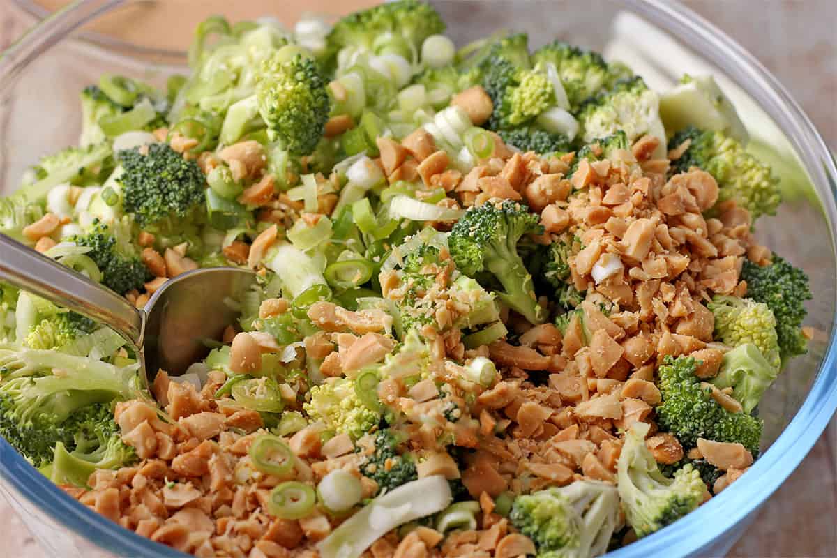 Broccoli, green onions, and peanuts are mixed in a glass bowl.