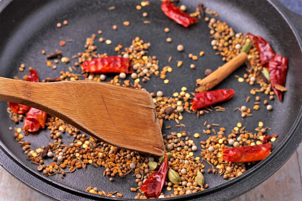 Whole spices and dried chilies are toasted in a cast iron pan and stirred with a wooden spoon.