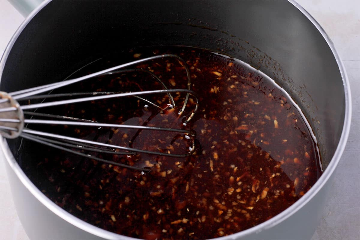 Sauce with minced garlic and ginger is whisked in a saucepan.