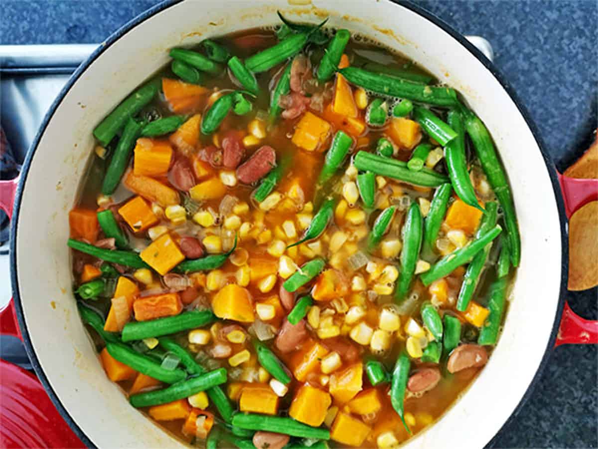 A pot of stew with green beans, sweeet potatoes, corn, and pinto beans in broth.