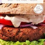 Close up of tempeh burger in bun with lettuce, onion, tomato, and vegan aioli. Text overlay of recipe title and website.