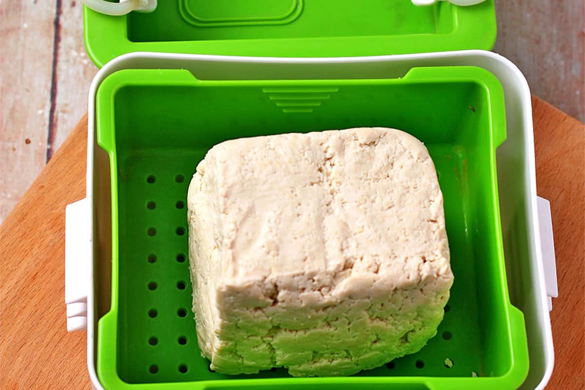 A block of tofu in a green tofu press.