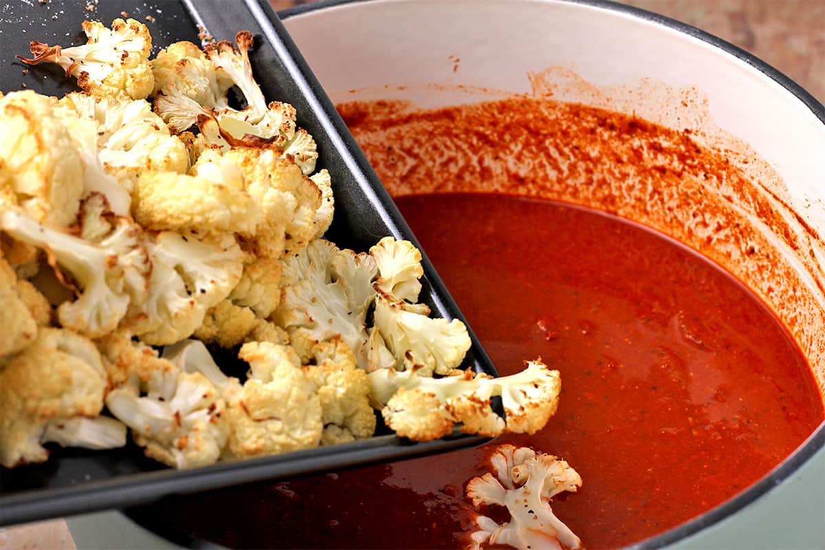 Roasted cauliflower on a baking tray is poured into vindaloo sauce.