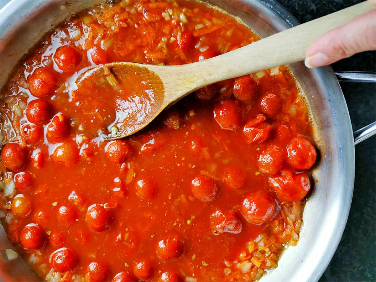 Canned cherry tomatoes in a pan with a wooden spoon.