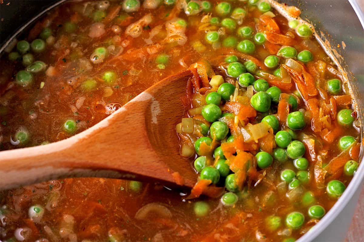 Frozen peas are stirred with carrots and broth in the Instant Pot.