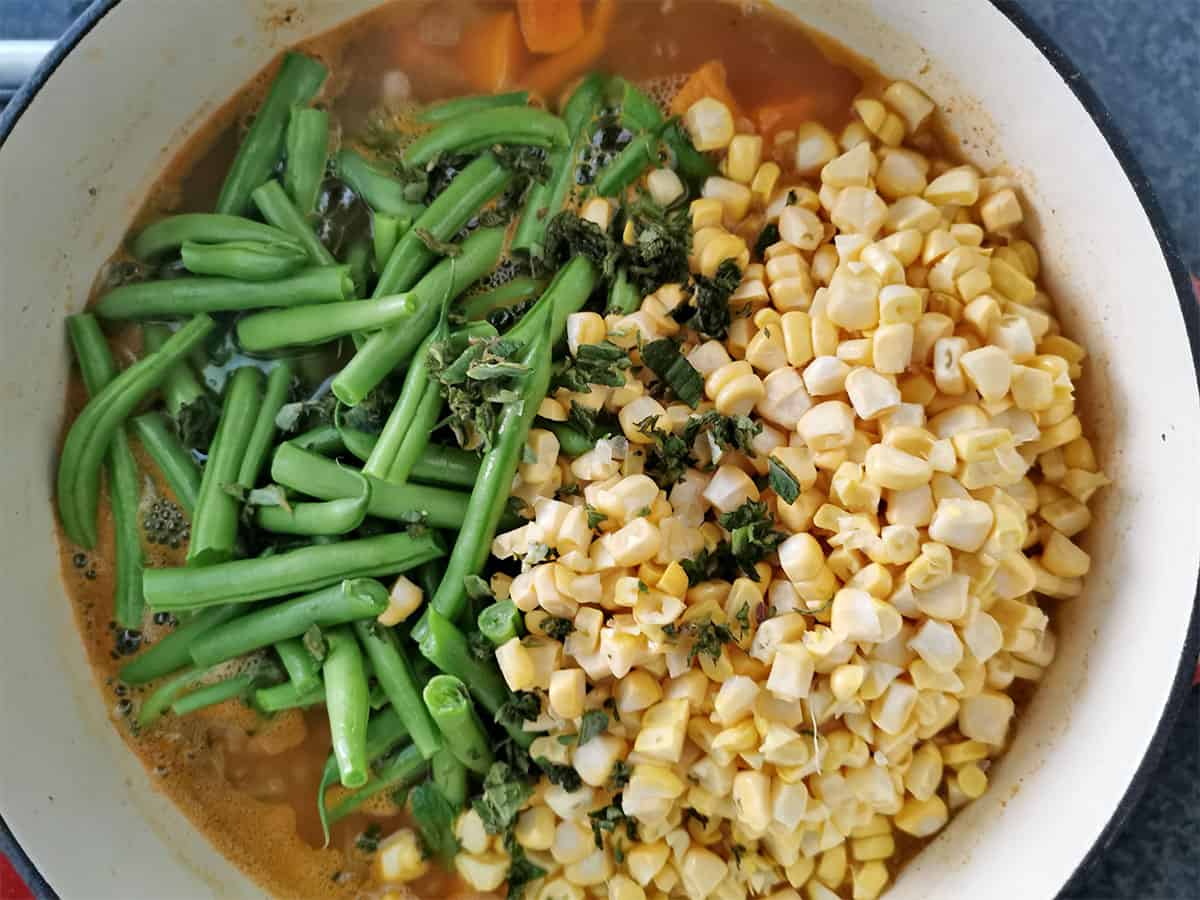 Green beans, corn kernels, and fresh oregano in a cooking pot.