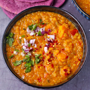 A bowl of red lentil dal with chopped red onion and cilantro.