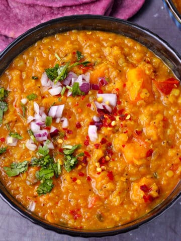 A bowl of red lentil dal with chopped red onion and cilantro.