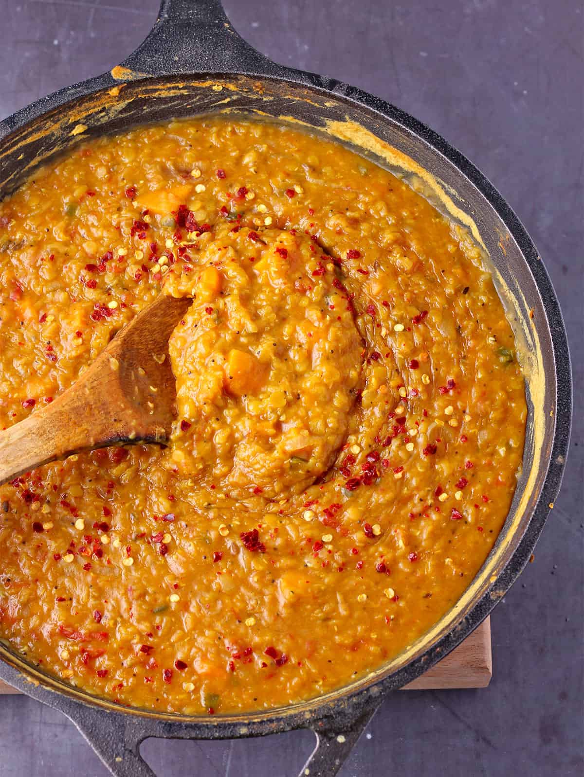 Lentil dal with sweet potatoes and tomatoes is stirred with a wooden spoon.