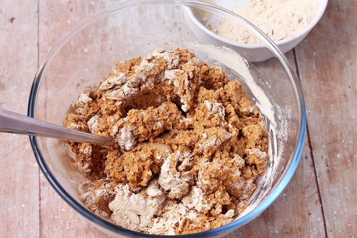 Vital wheat gluten is added to tempeh burger mixture in a glass bowl.