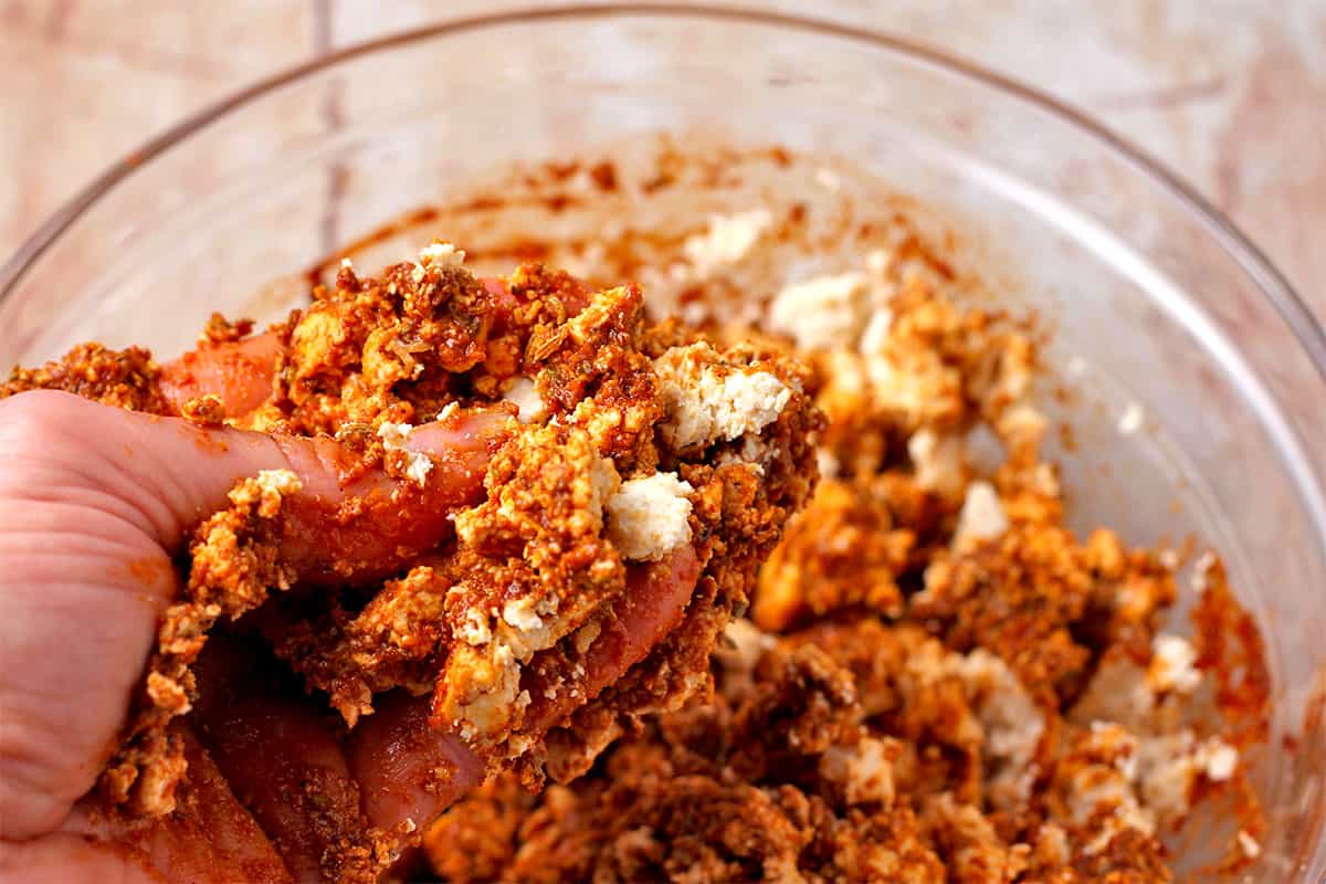 Crumbled tofu is mixed with marinade with hand.