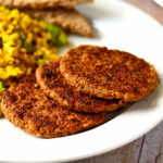 Three vegan tempeh breakfast sausage patties on a white plate with tofu scramble and toast.