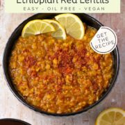 A black bowl is filled with Ethiopian red lentils with lemon slices on top.