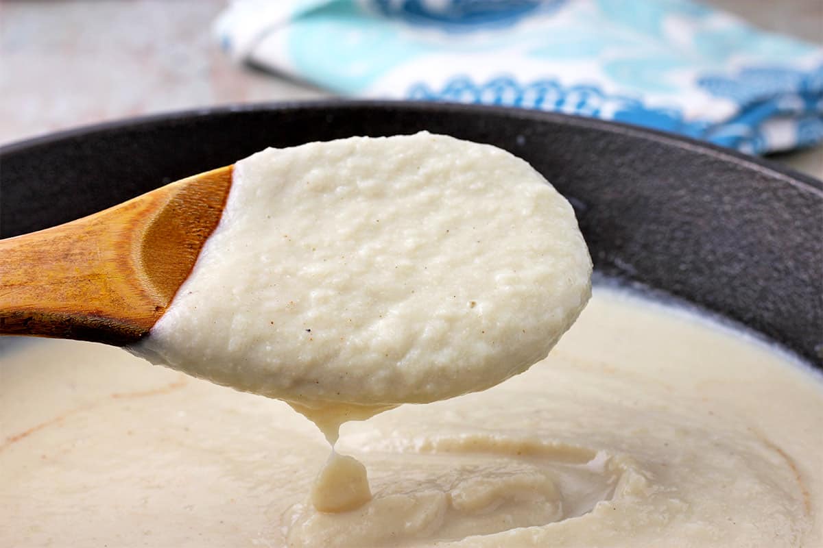 A spoonful of cauliflower bechamel sauce is held of a pot of sauce.