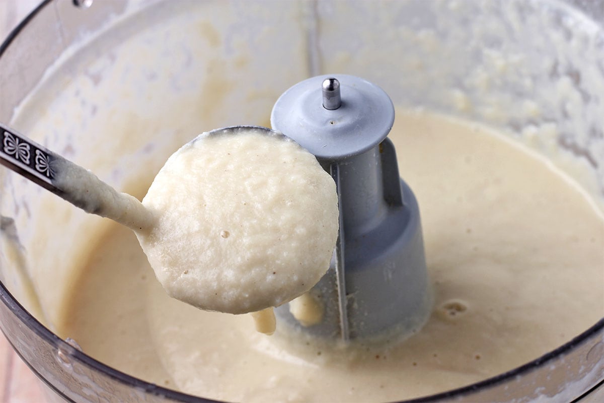 Blended white sauce in a small ladle held over a food processor.