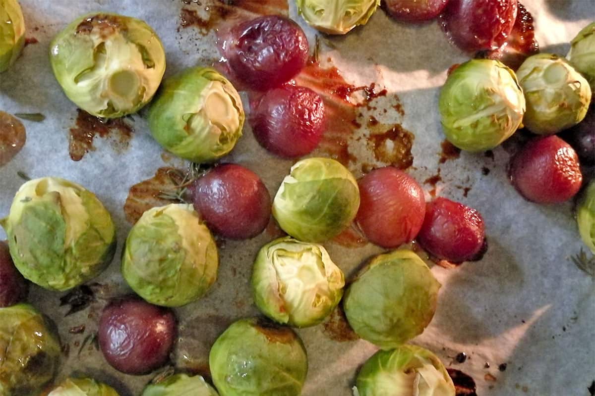 Roasting Brussels sprouts and red grapes on parchment paper.