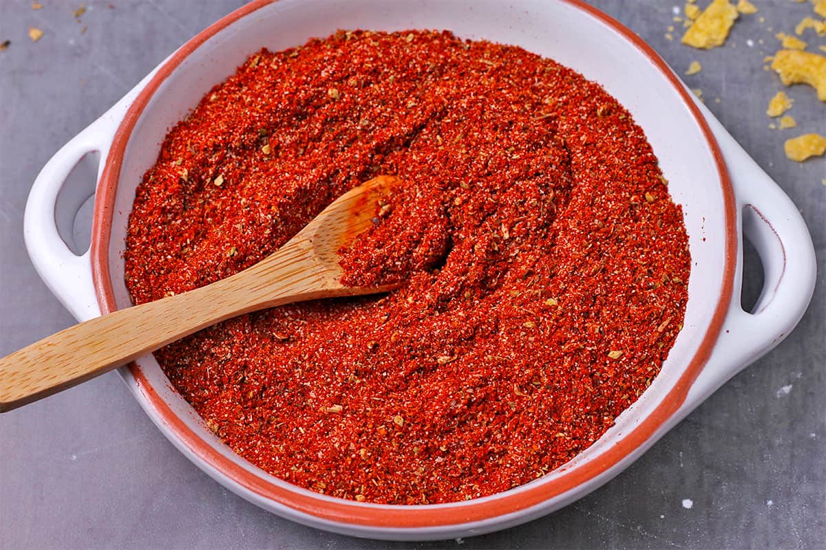 Chili powder in a white dish and a small wooden spoon.