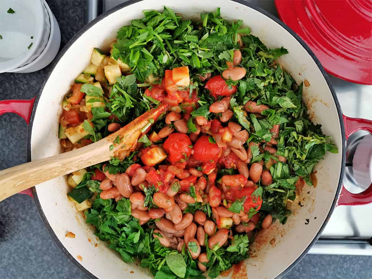 Tomatoes, pinto beans, and cilantro added to a cooking pot.