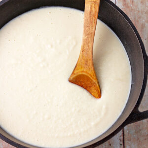 White bechamel sauce in a cast iron pan with a wooden spoon in the pan.