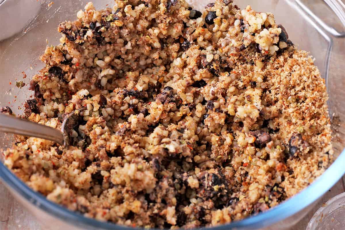 Black beans, breadcrumbs, and cooked bulgur are mixed with a spoon.