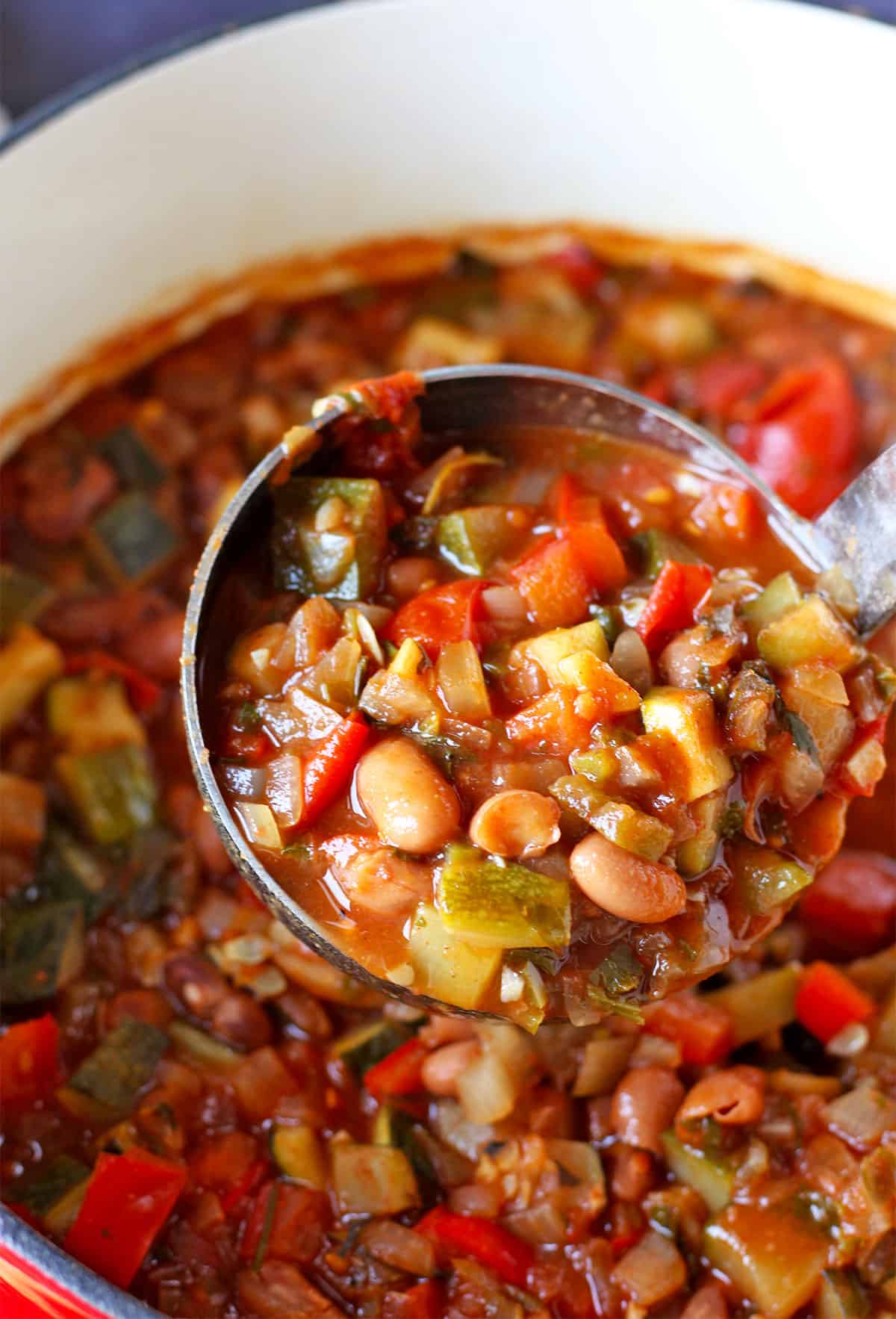 Chili with zucchini, pinto beans, tomatoes, and red pepper is ladled from a cooking pot.