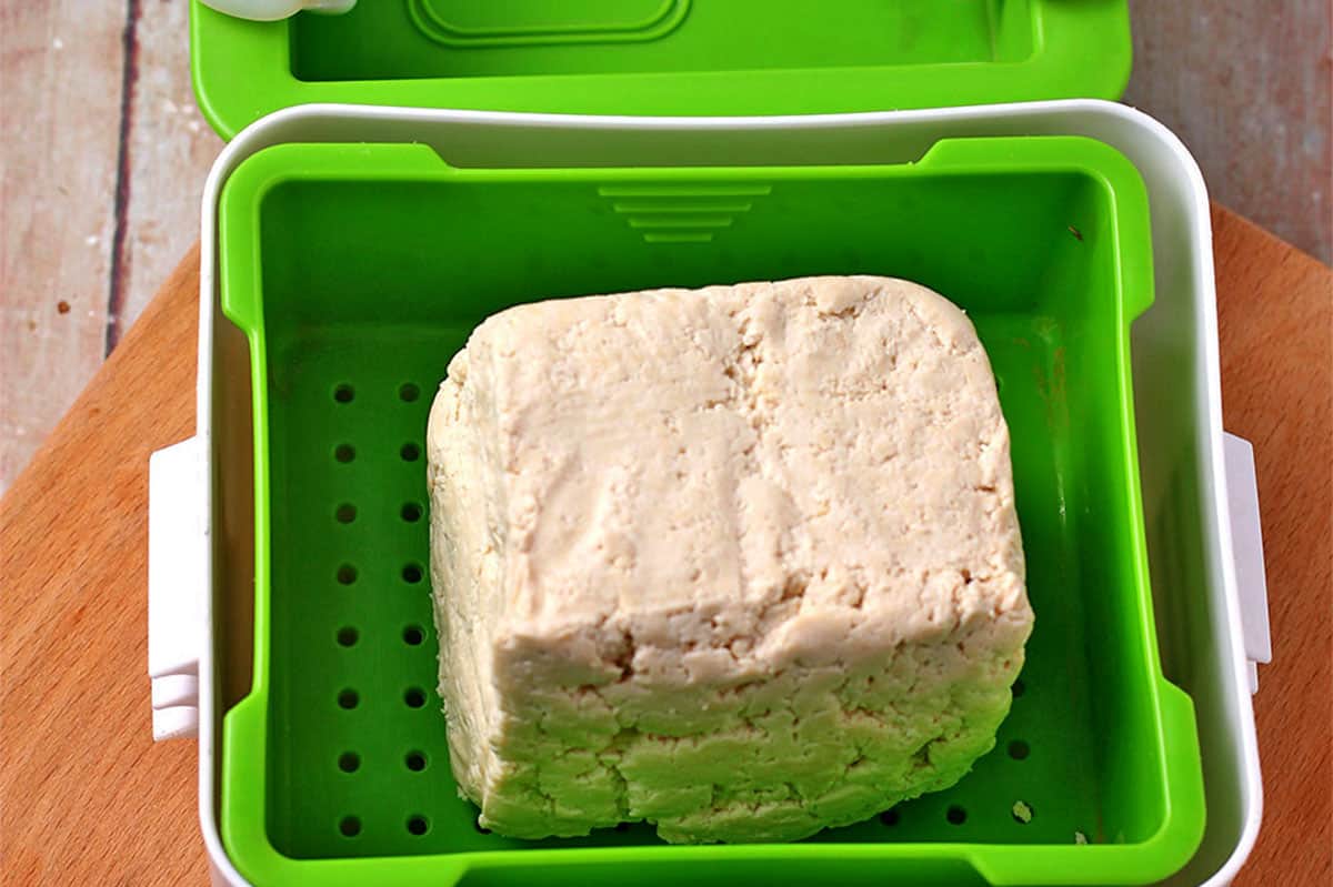 A block of tofu in a green tofu press.