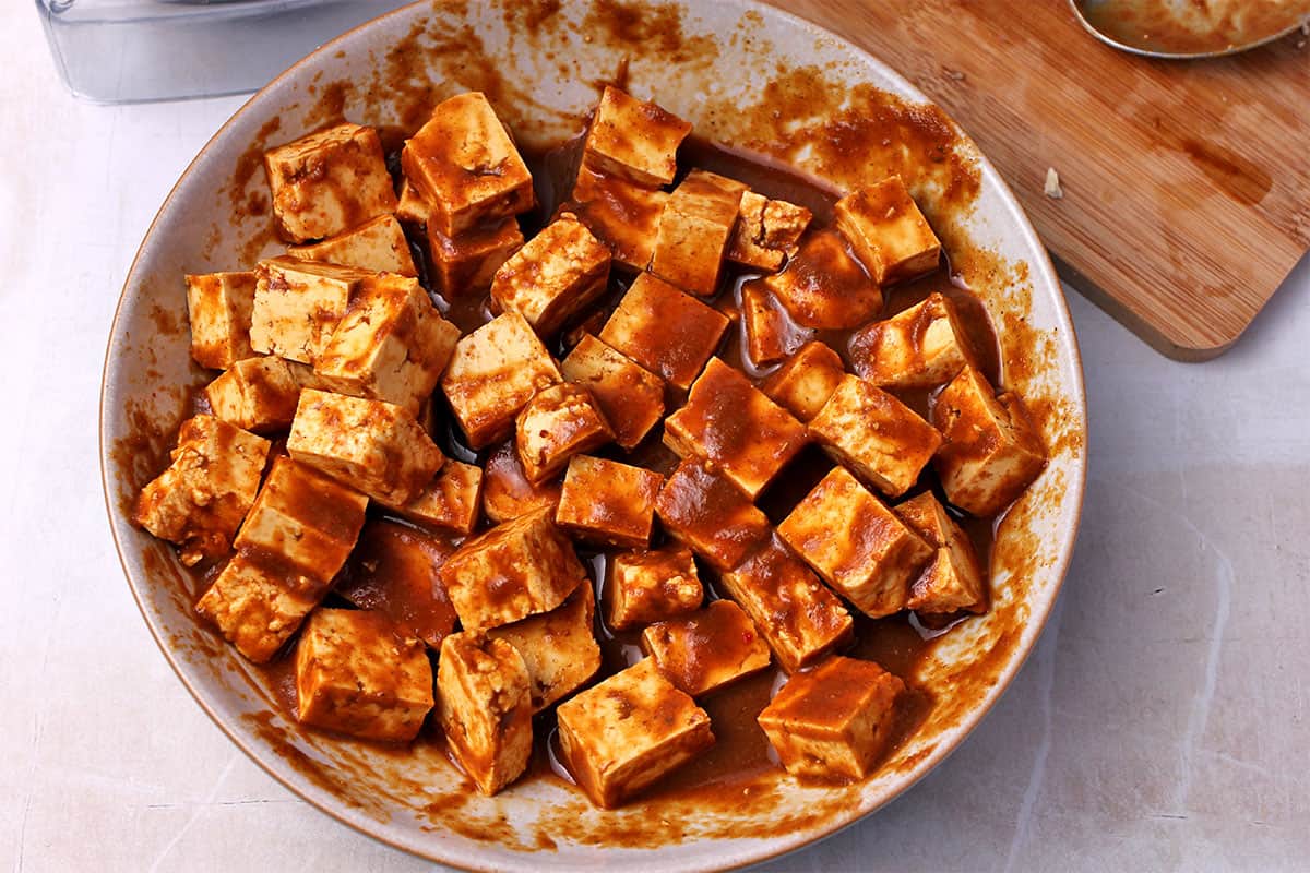 Tofu cubes are marinated in a dish.
