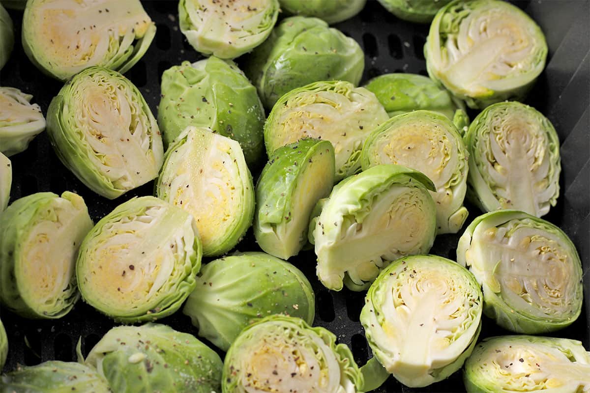 Brussels are cut in half with salt and pepper and placed in an air fryer basket.