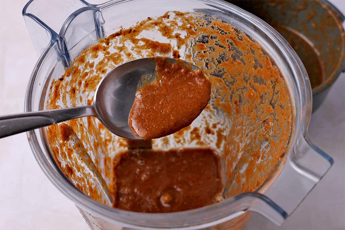Jerk marinade in a spoon held over a blender.