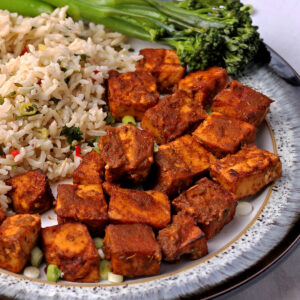 Jerk tofu cubes on a plate with rice and green onions.