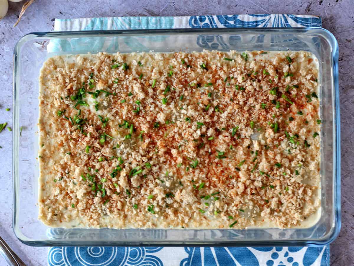 Creamed onions tipped with breadcrumbs and chives in a glass baking dish.