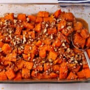 Roasted sweet potatoes with chopped pecans and orange zest in a glass baking dish with a spoon.