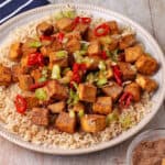 Salt and Pepper tofu cubes with green onions and chili over brown rice on a plate.