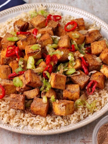 Salt and Pepper tofu cubes with green onions and chili over brown rice on a plate.